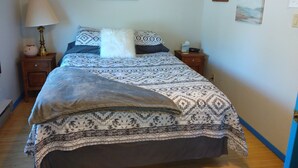 Un letto ben rifatto con biancheria a motivi decorativi, una lampada da comodino e un piccolo tavolino con una scatola di fazzoletti e un telecomando.