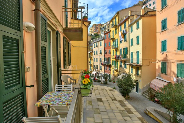 Une rue étroite bordée de bâtiments aux couleurs vives, une table avec des chaises et un panier de fleurs.