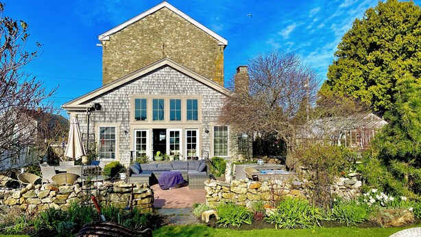 A stone building with a large porch, surrounded by a well-maintained garden and outdoor seating area.