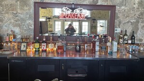 A bar area with a mirror reflecting a person, surrounded by various bottles and glasses.