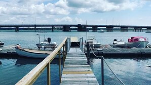 A wooden dock leading to a marina with boats docked, a bridge in the background, and a clear sky.