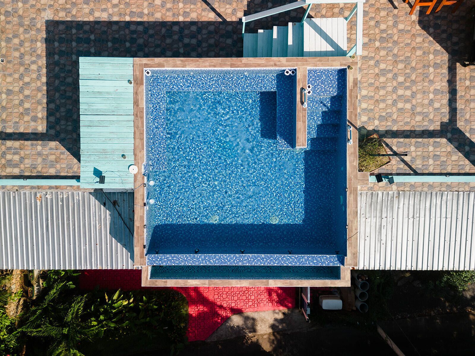Vue aérienne d’une piscine rectangulaire entourée d’une terrasse carrelée.
