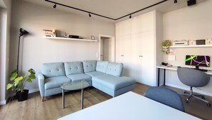 A modern living room with a light blue sectional sofa, a glass coffee table, a white desk with a computer, and a grey office chair. - Recently refurbished flat, very well connected and close to Mauerpark (Berlin)
