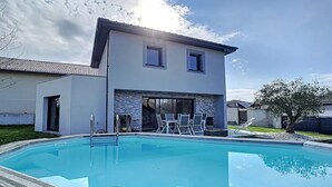 Et moderne hus i to etager med swimmingpool, udendørs møbler og en stenvæg.