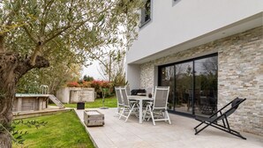 En moderne udendørs terrasse med et bord, stole og en loungeseng, samt en stenvæg.
