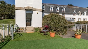 A white building with a small porch and steps leading to the entrance. There is a large bush in front of the building. - La Tour du Castel Beach - 200m de la plage (Moëlan-sur-Mer)