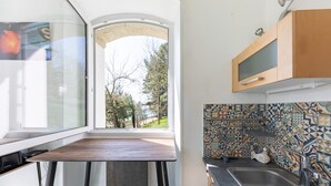 A compact kitchen with a window, a wooden table, a bench, and a tiled backsplash. - La Tour du Castel Beach - 200m de la plage (Moëlan-sur-Mer)