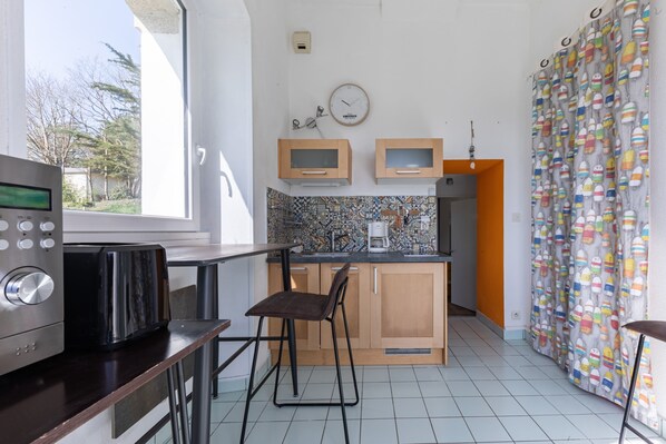 A compact kitchen with a microwave, toaster, and a small coffee maker. There is a window providing natural light and a view of trees outside.