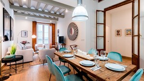 A dining area with a wooden table set for four, surrounded by teal chairs, and a large pendant light above.