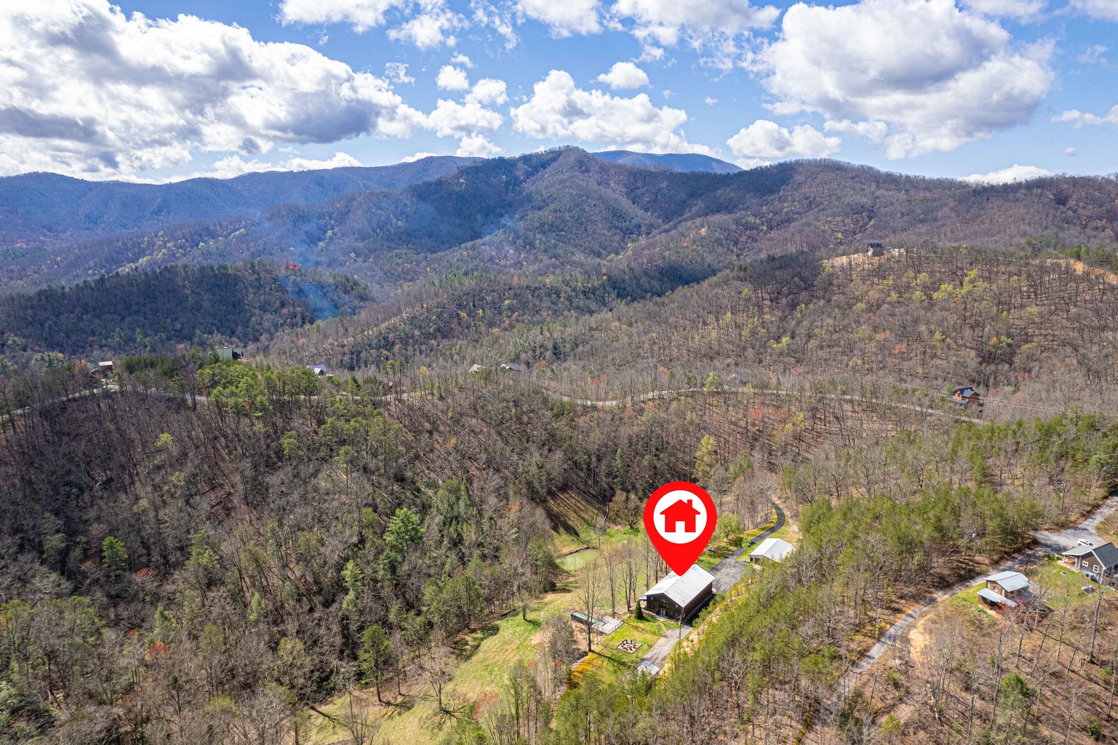 A remote cabin surrounded by forested mountains, with a clear sky and a red location marker.