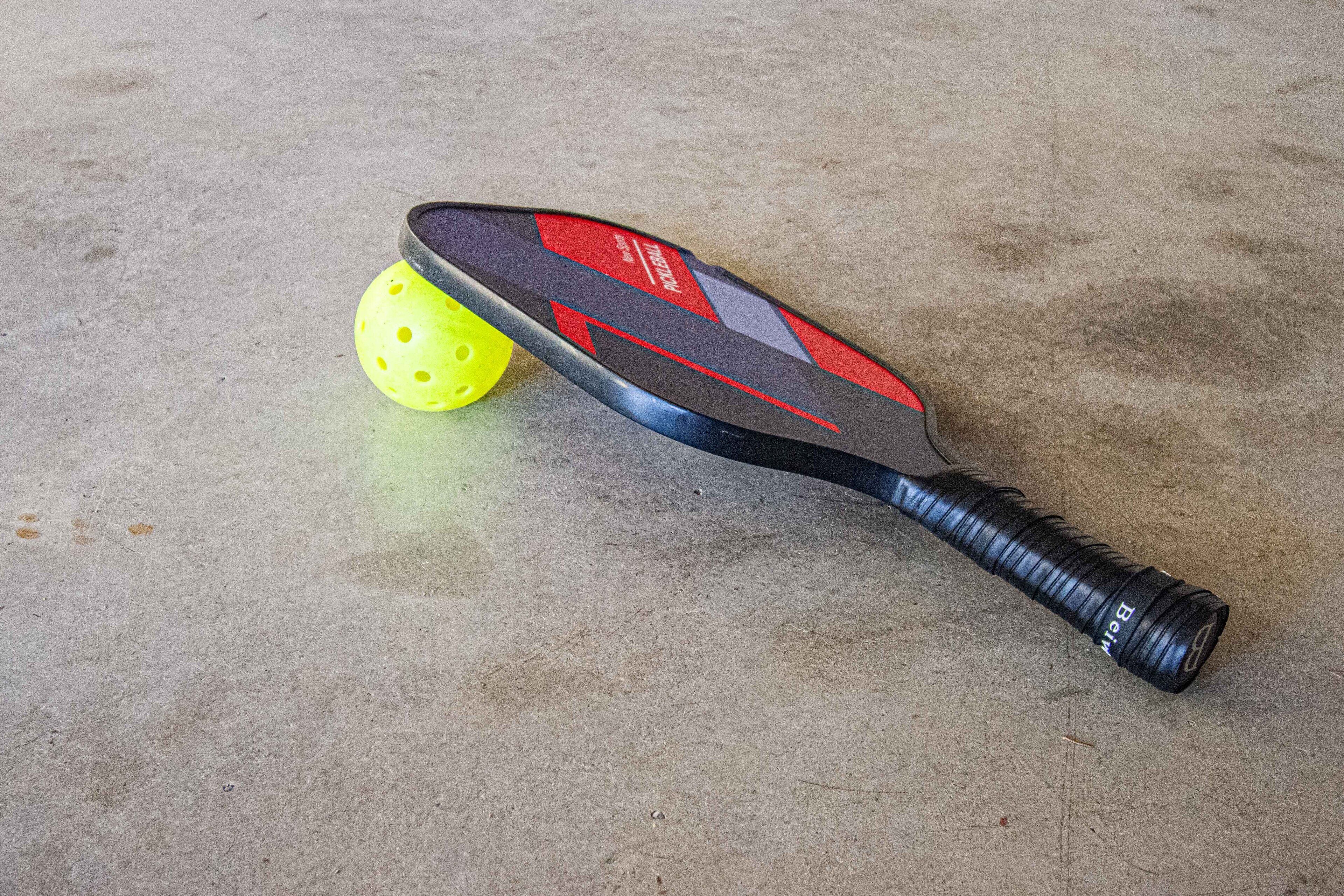 Une batte de cricket et une balle jaune sur un sol en béton.