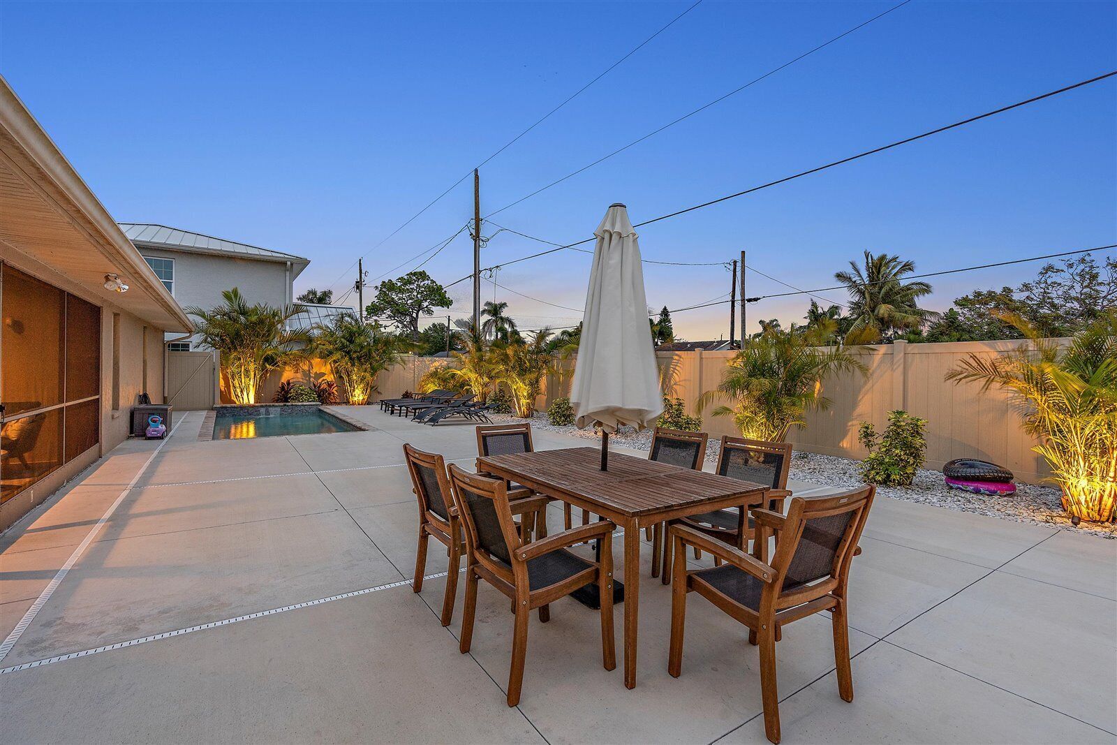 A patio with a wooden table and chairs, a swimming pool, and various plants.