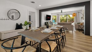 A modern living room with a dining table, sofa, and TV. - Sea Esta | Private Saltwater POOL + Putting Green! (Sarasota)