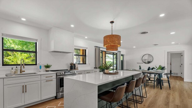 A modern kitchen with white cabinetry, a large island, bar stools, and a hanging light fixture. - Sea Esta | Private Saltwater POOL + Putting Green! (Sarasota)