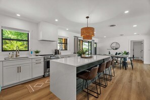 A modern kitchen with white cabinetry, a large island, bar stools, and a hanging light fixture.