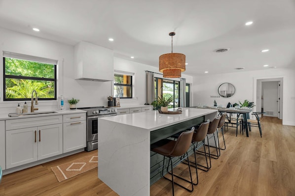 A modern kitchen with white cabinetry, a large island, bar stools, and a hanging light fixture.