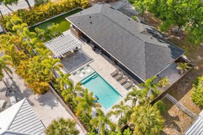 A large building with a swimming pool, surrounded by palm trees and a garden.