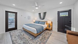 Ein modernes Schlafzimmer mit Bett, Nachttischlampen, Deckenventilator und einer dunklen Tür.