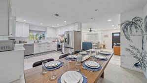 Eine moderne Küche mit weißen Schränken, einem Edelstahlkühlschrank und einer Essecke für sechs Personen, gedeckt mit blauen Untersetzern und weißen Tellern.