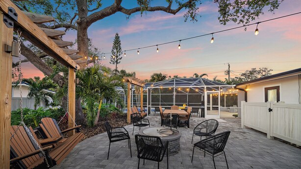 Eine Terrasse im Freien mit einer Holzpergola, Lichterketten und einem Gewächshaus aus Glas.