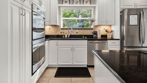 Cocina moderna con armarios blancos, electrodomésticos de acero inoxidable, encimera negra y ventana con vistas a zonas verdes.