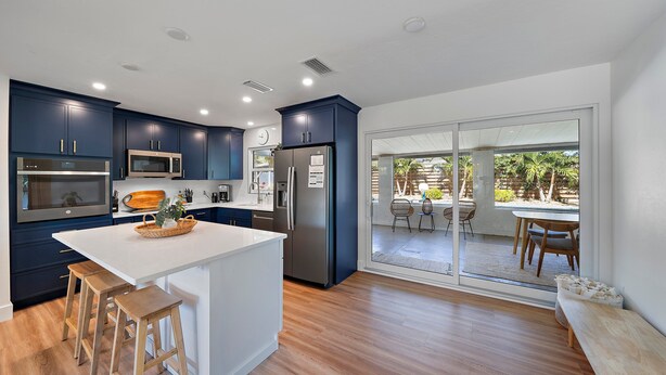 Une cuisine moderne avec des meubles bleu foncé, un îlot central blanc et des tabourets en bois.