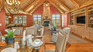 A spacious living area with a high ceiling, stone fireplace, and a large TV. - Kountry Lane Stables | Horse Farm w/ HOT TUB + Fire Pit! (Wakarusa)