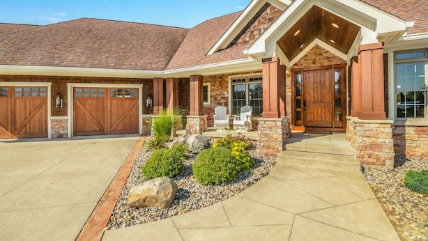 A two-story house with a stone facade, a covered porch, and a garage with two doors. - Kountry Lane Stables | Horse Farm w/ HOT TUB + Fire Pit! (Wakarusa)