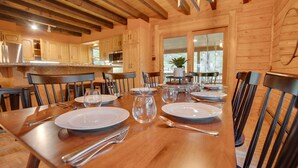 Une table de salle à manger en bois, mise avec des assiettes, des couverts et un pichet, dans une pièce aux murs et aux poutres apparentes en bois.