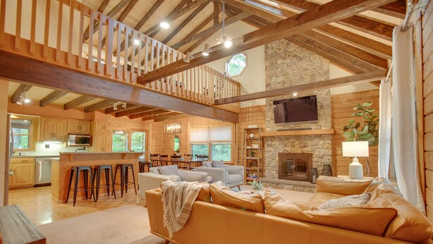 Un vaste espace de vie doté d’un plafond haut, de poutres en bois, d’une cheminée en pierre et d’un coin salon confortable.