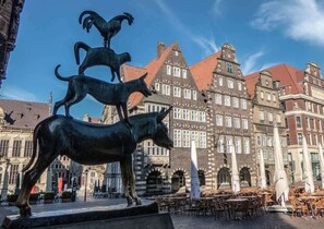 A public square with a sculpture of animals, historic buildings, and outdoor seating.