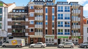 Un immeuble résidentiel à plusieurs étages doté de balcons, un restaurant appelé « Kabul Restaurant » et un fourgon arborant le logo « STB ».