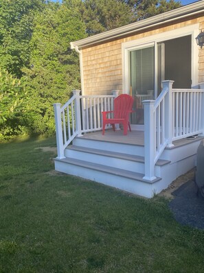 Relax on the covered porch with a comfortable Adirondack chair, surrounded by a well-maintained lawn and lush trees.