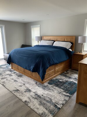 A bedroom with a wooden bed, two bedside tables, a patterned rug, and a window with blinds.