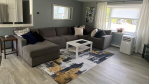 A modern living room with a sectional sofa, a coffee table, and a dining area with a window. - Home away  Harwich (Harwich)