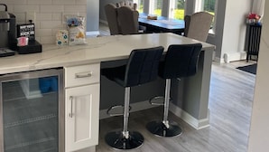 A modern kitchen with a central island, bar stools, and a dining area with a view. - Home away  Harwich (Harwich)