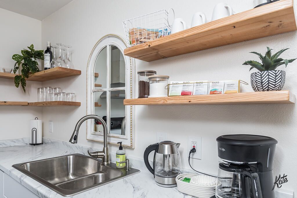 Eine moderne Küche mit einer Edelstahlspüle, einem Wasserkocher, einer Kaffeemaschine und Holzregalen mit verschiedenen Gegenständen.