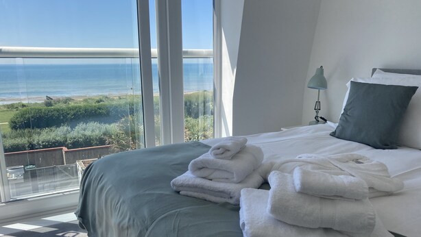 A bedroom with a large window overlooking a coastal landscape, a neatly made bed with white linens, and a green accent wall. - Stunning, newly refurbished, beachfront townhouse in Rustington (Rustington)