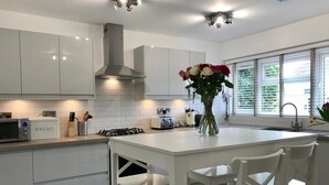A modern kitchen with white cabinetry, a central island with chairs, a gas stove, and a microwave. - Stunning, newly refurbished, beachfront townhouse in Rustington (Rustington)