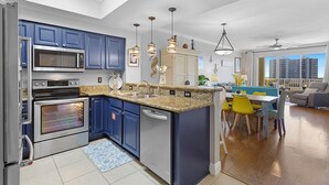 A modern kitchen with built-in appliances, a dining area with yellow chairs, and a view of the city through large windows.