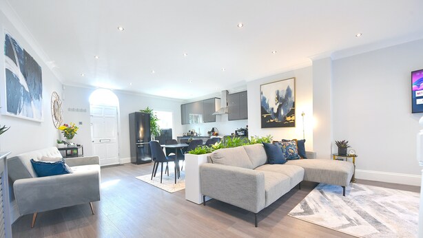 A modern living room with a grey sofa, a dining area, and a kitchen in the background.