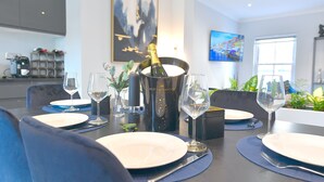 A dining table set with plates, cutlery, and wine glasses, with a bottle of champagne in a bucket.