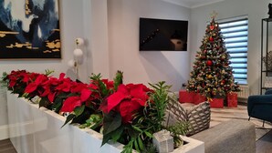 A modern living room with a Christmas tree, poinsettia plants, and a large abstract painting on the wall.