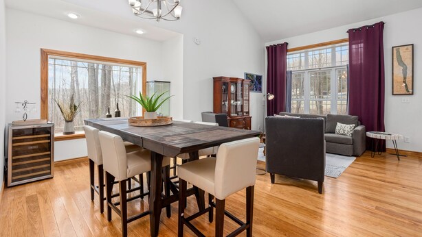 Un salon spacieux avec une table à manger en bois, des sièges confortables, un ventilateur de plafond et de grandes fenêtres avec des rideaux.