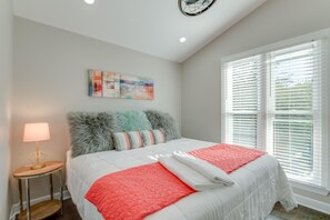 Um quarto com cama, mesa de cabeceira, abajur, janela com persianas e luminária de teto.