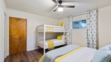 A bedroom with a bunk bed, a ceiling fan, a window with curtains, and a wooden door.