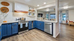 A modern kitchen with blue cabinets, stainless steel appliances, and a wooden floor.