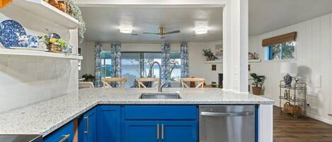 A modern kitchen with blue cabinets, a stainless steel dishwasher, and a granite countertop.