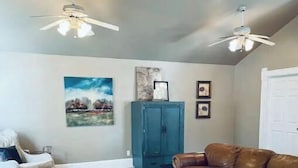 A living room with a brown leather sofa, a white armchair, a teal cabinet, and two ceiling fans. - Beautiful home, historic property- downtown Nampa (Nampa)