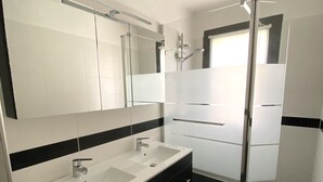 Ein modernes Badezimmer mit einem Doppelwaschtisch, einem großen Spiegel und einer Duschkabine aus Glas.
